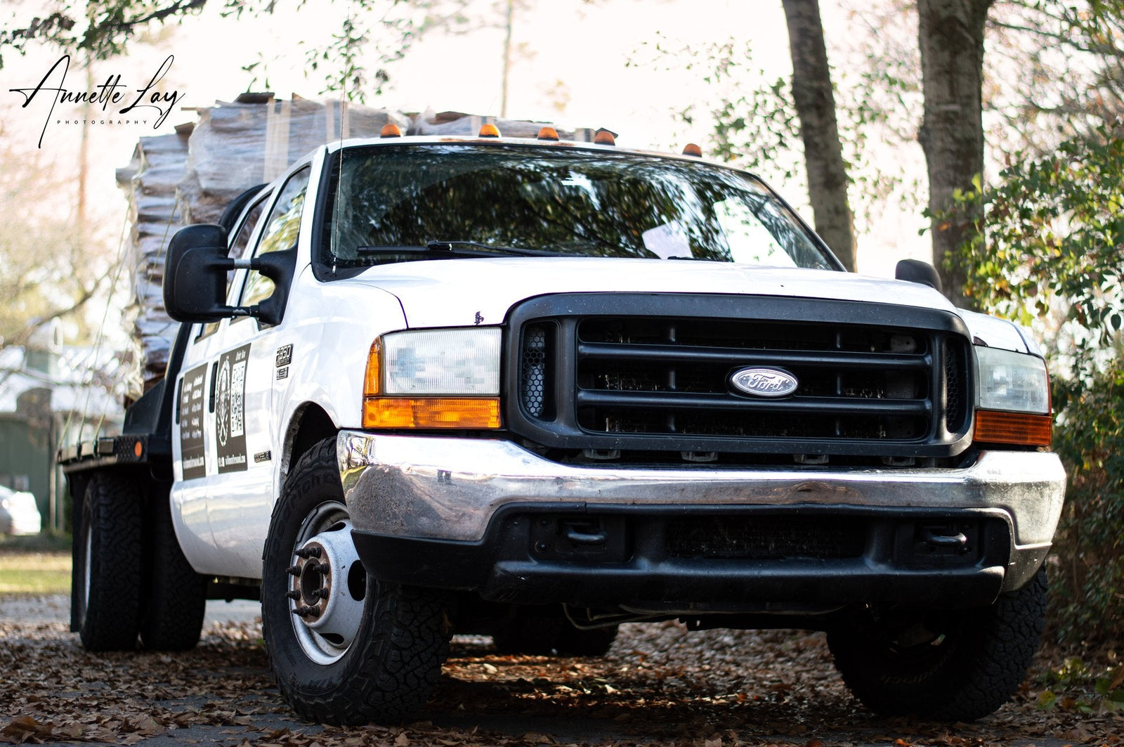 White Ford truck with a bed of construction materials on a road.